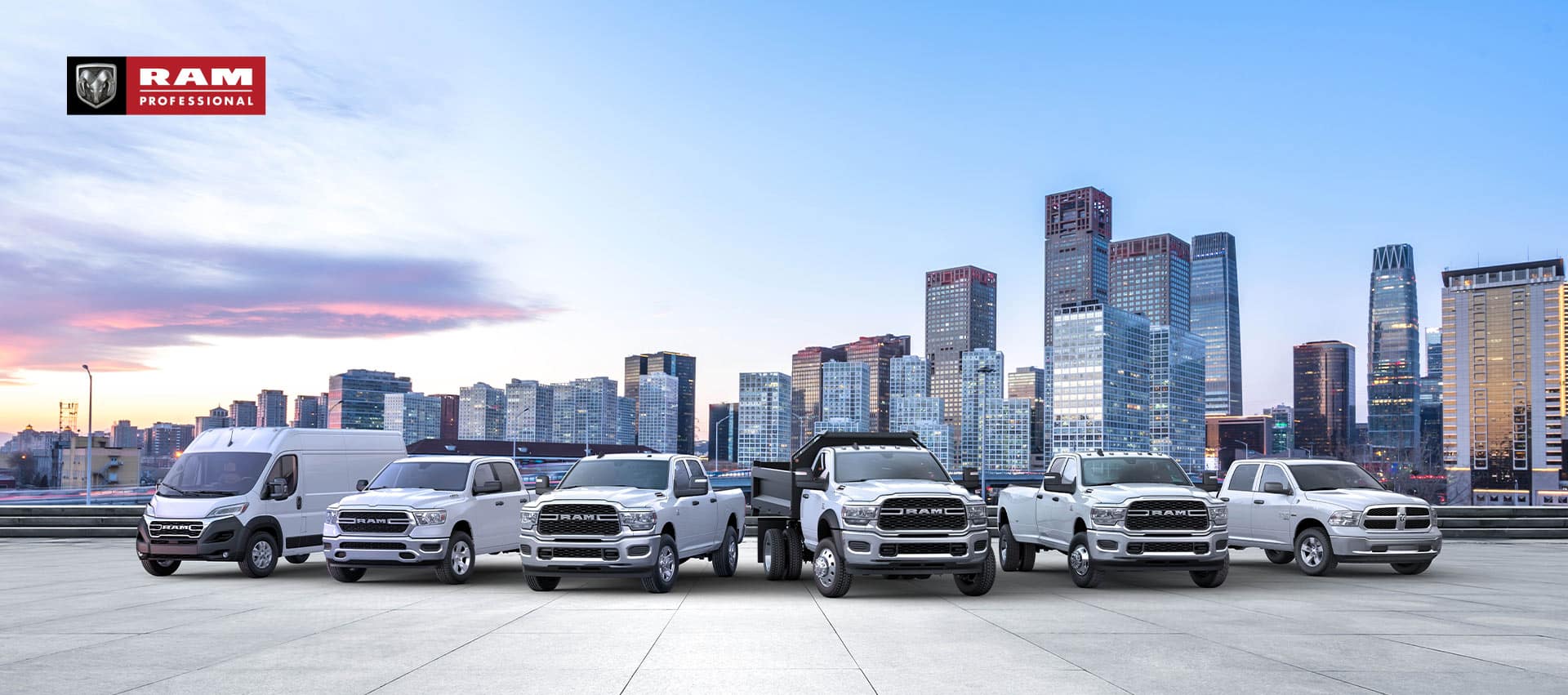 The Ram Brand lineup, all in white, parked side-by-side with a cityscape at dusk in the background. Beginning on the left: a 2023 Ram ProMaster 3500 High Roof Cargo Van, 2022 Ram ProMaster City Cargo Van, 2023 Ram 1500 Tradesman Crew Cab, 2023 Ram 5500 Tradesman Regular Cab with dump body, 2023 Ram 3500 Tradesman Crew Cab and 2023 Ram 1500 Classic Regular Cab. Ram Professional.