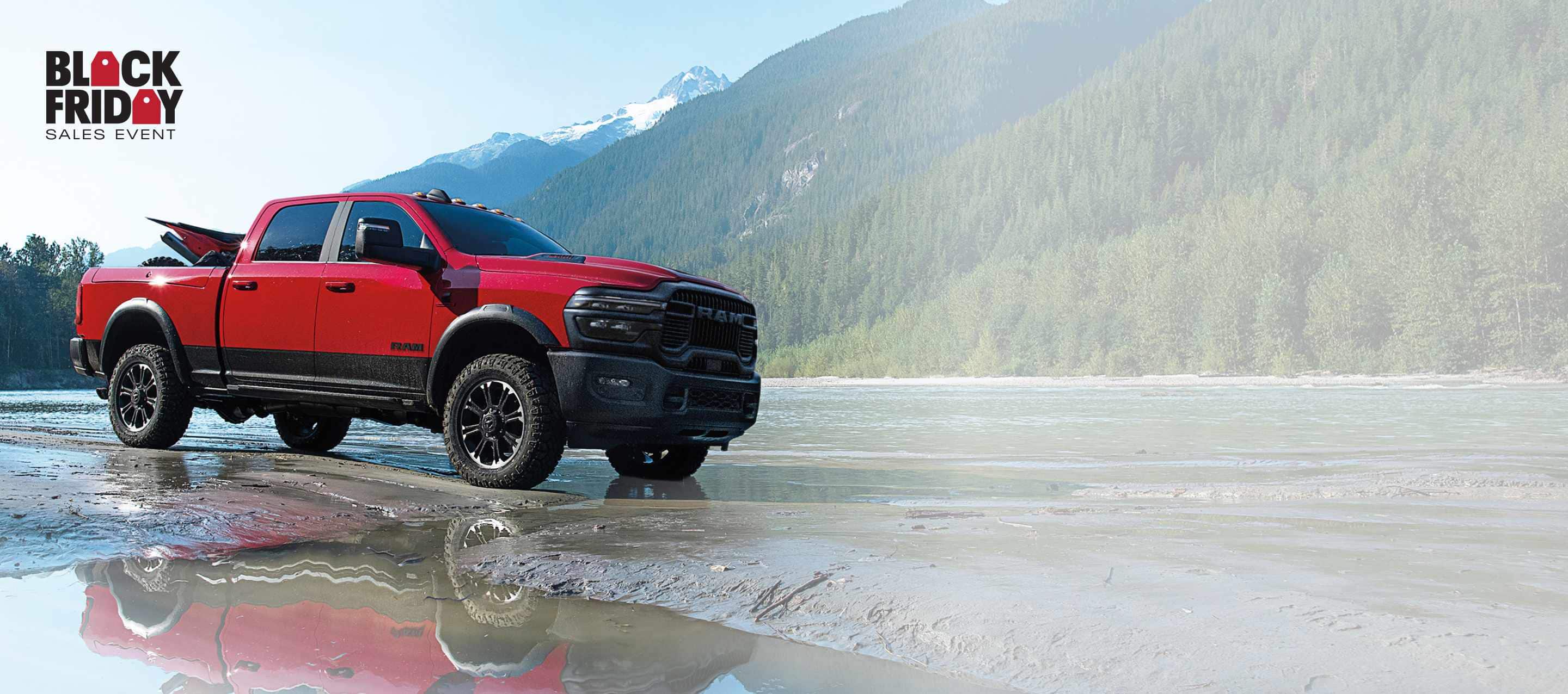 A white 2025 Ram 2500 Tradesman 4x4 Crew Cab towing a front end loader on a flatbed trailer through a muddy construction site. Black Friday Sales Event.