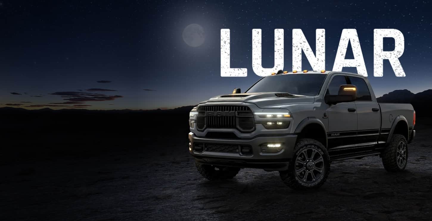 A driver-side front angle of a light gray 2026 Ram 2500 Lunar 4x4 Crew Cab with a dark background of sea and sky after sunset. Lunar.