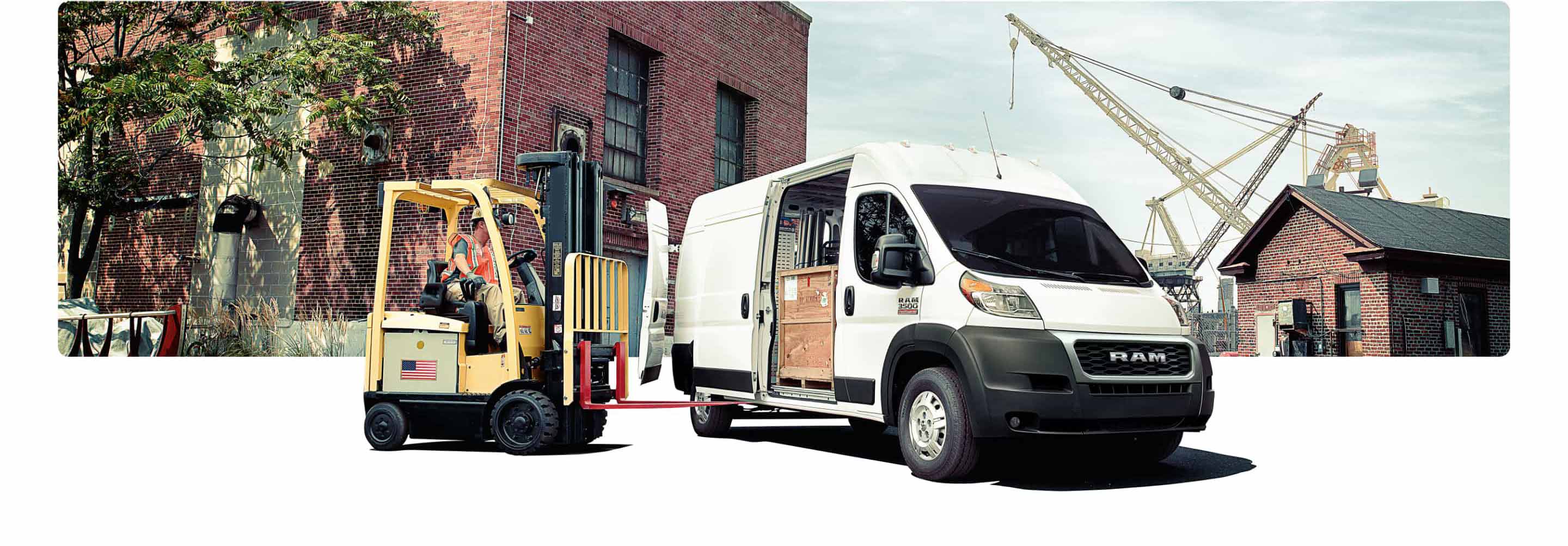 The 2021 Ram ProMaster parked in front of a warehouse with a forklift approaching its open side door to unload the boxes within.