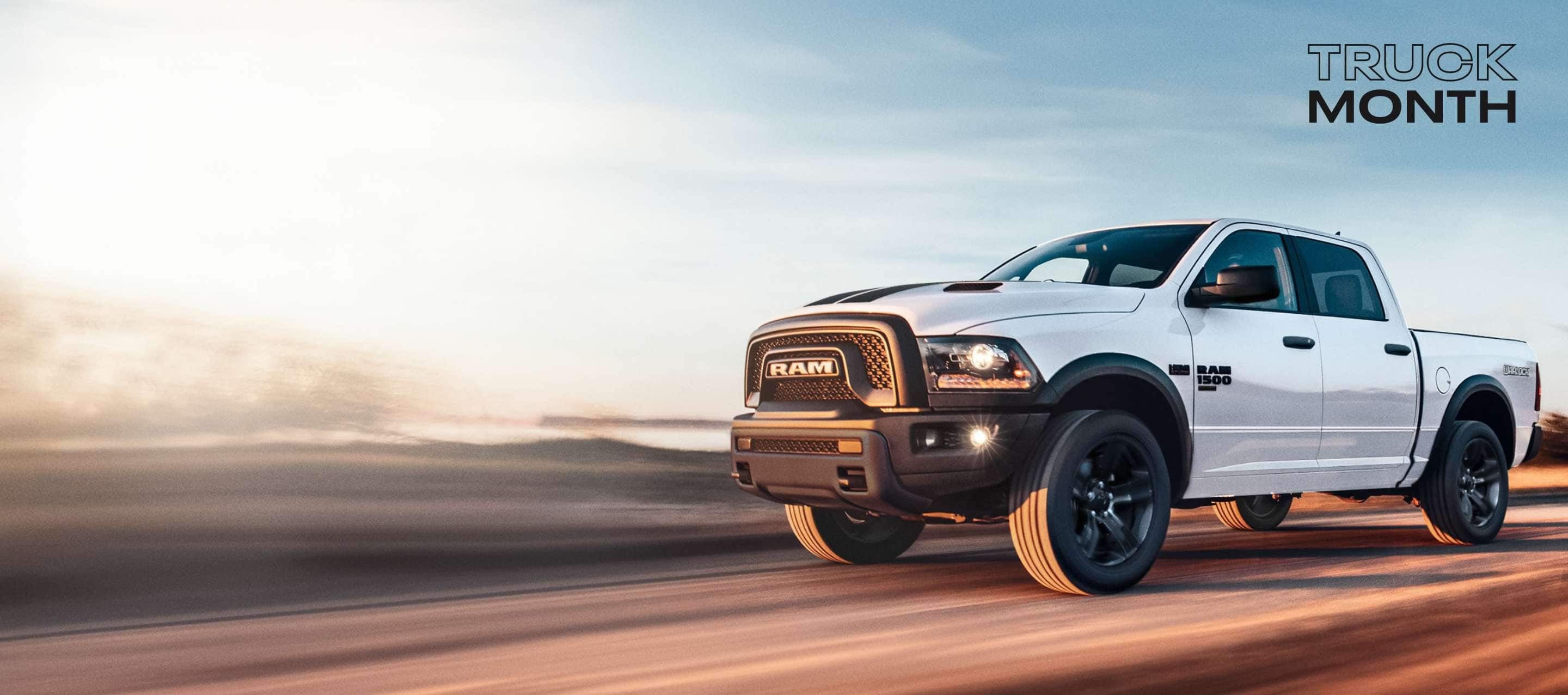 A white 2024 Ram 1500 Classic Warlock 4x4 Crew Cab traveling down a highway. Truck Month Sales Event.