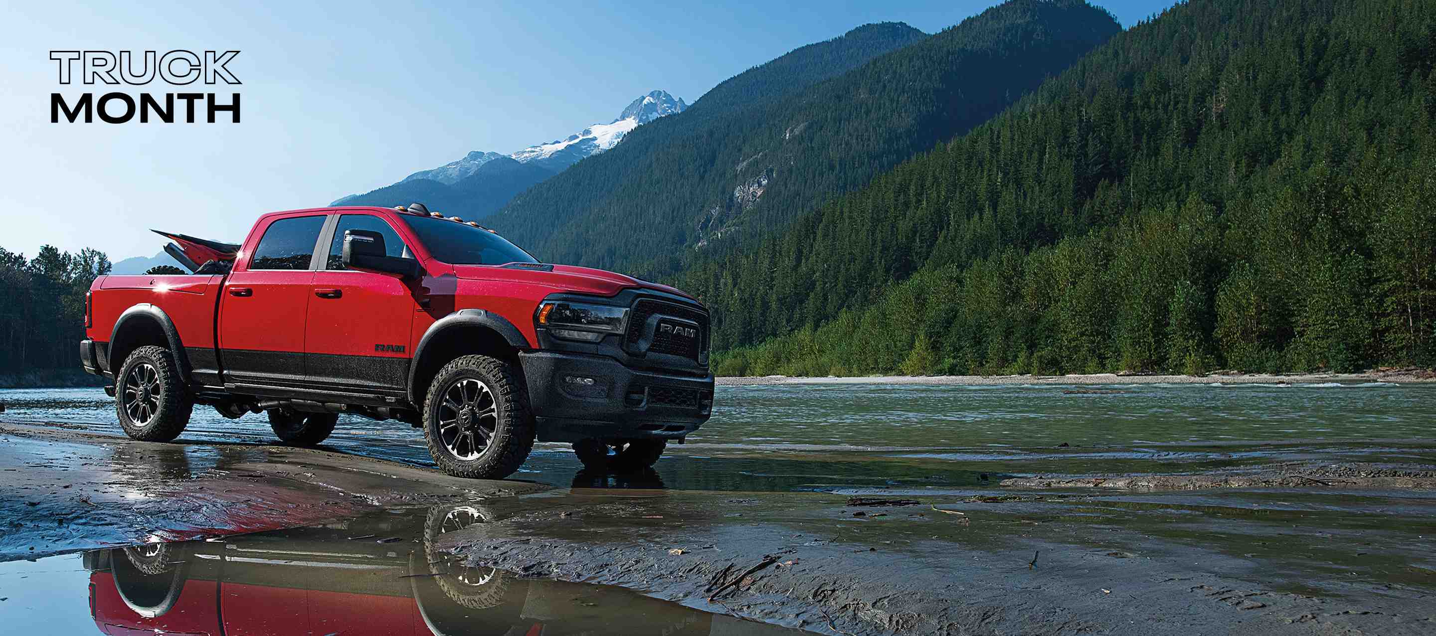 A red 2024 Ram 2500 Rebel 4x4 Crew Cab with an ATV in its pickup box, and mountains in the background. Truck Month.