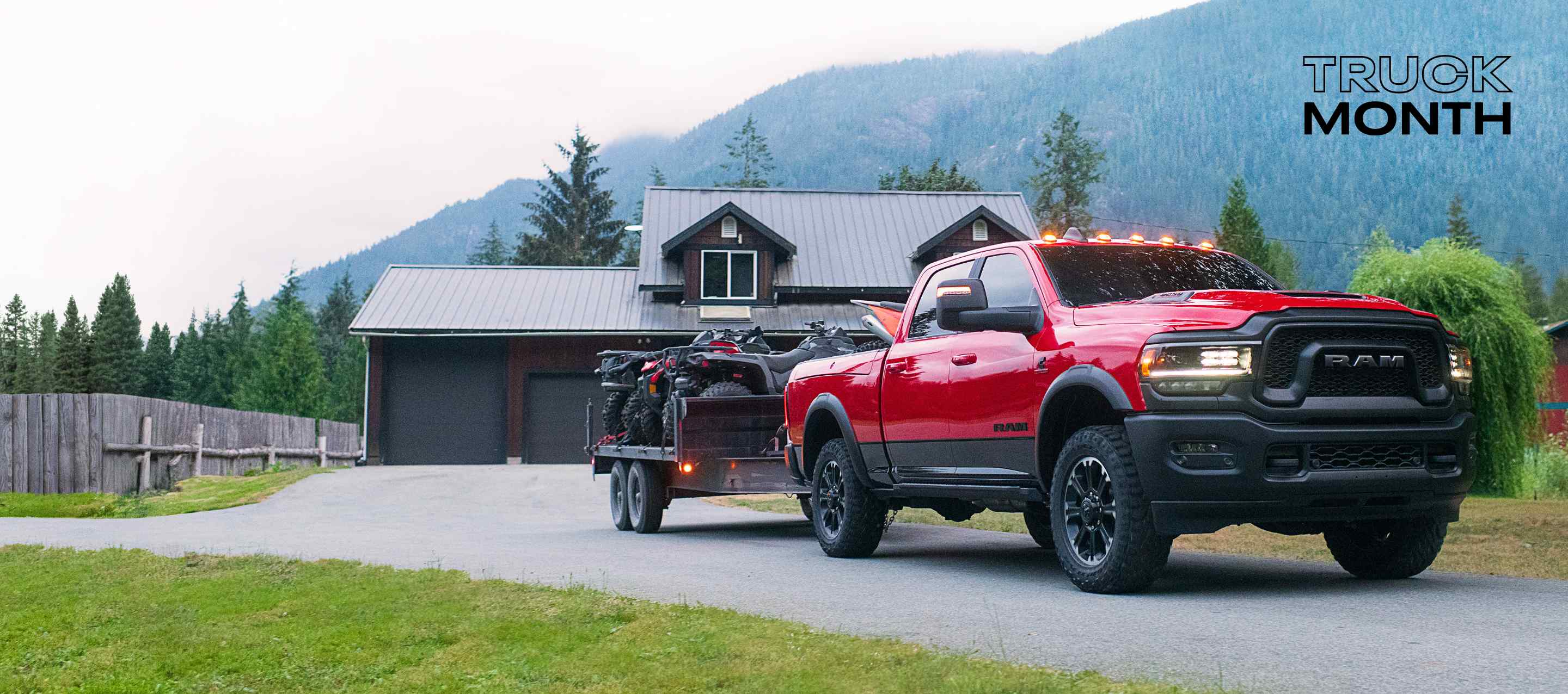 A red 2024 Ram 2500 Rebel 4x4 Crew Cab towing two ATVs as it pulls out of the driveway of a home. Truck Month Sales Event.