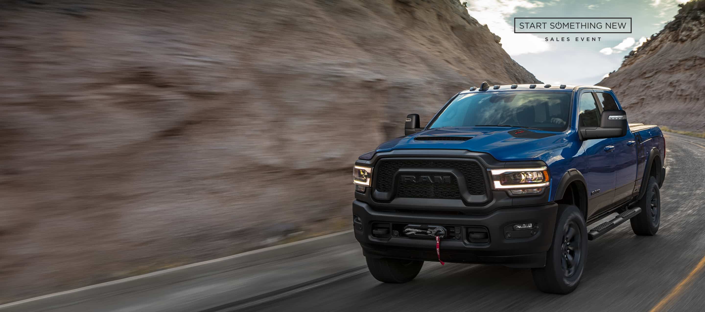 A blue 2024 Ram 2500 Power Wagon Crew Cab taking a curve on a mountain highway. The Start  Something New Sales Event.