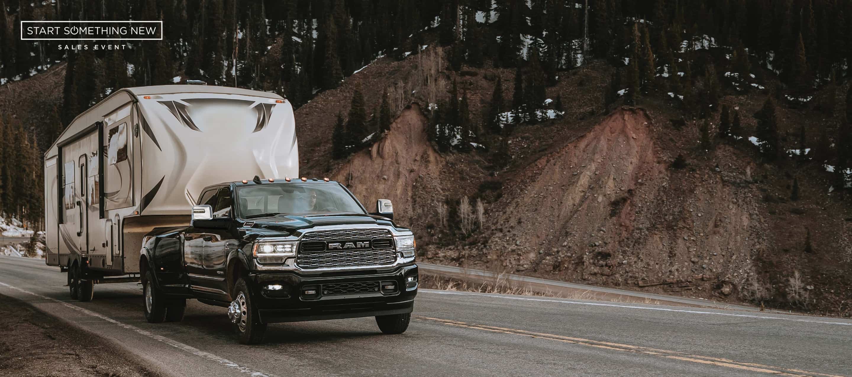 A black 2024 Ram 3500 Limited Crew Cab traveling down a highway, towing a fifth wheel travel trailer. The Start Something New Sales Event.