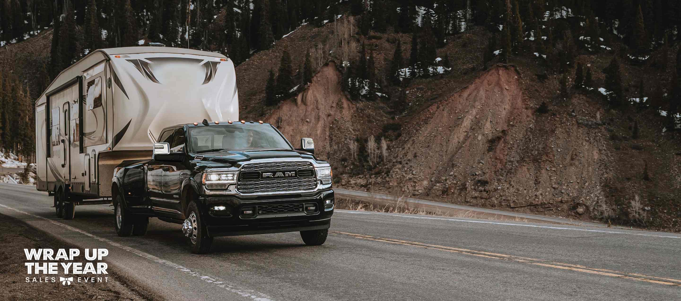 A black 2024 Ram 3500 Limited Crew Cab traveling down a highway, towing a fifth wheel travel trailer. The Wrap Up The Year Sales Event.