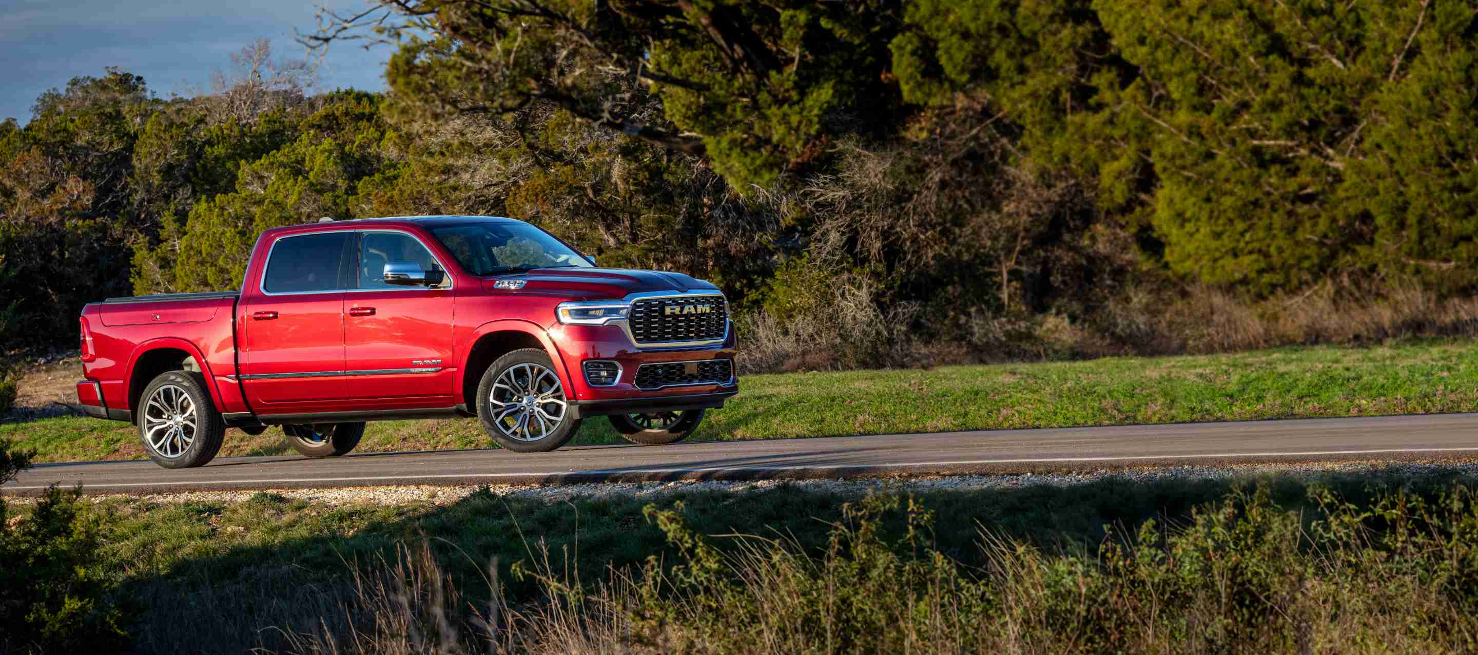 A passenger-side profile of a red 2025 Ram 1500 Tungsten Crew Cab parked on the side of a country road.