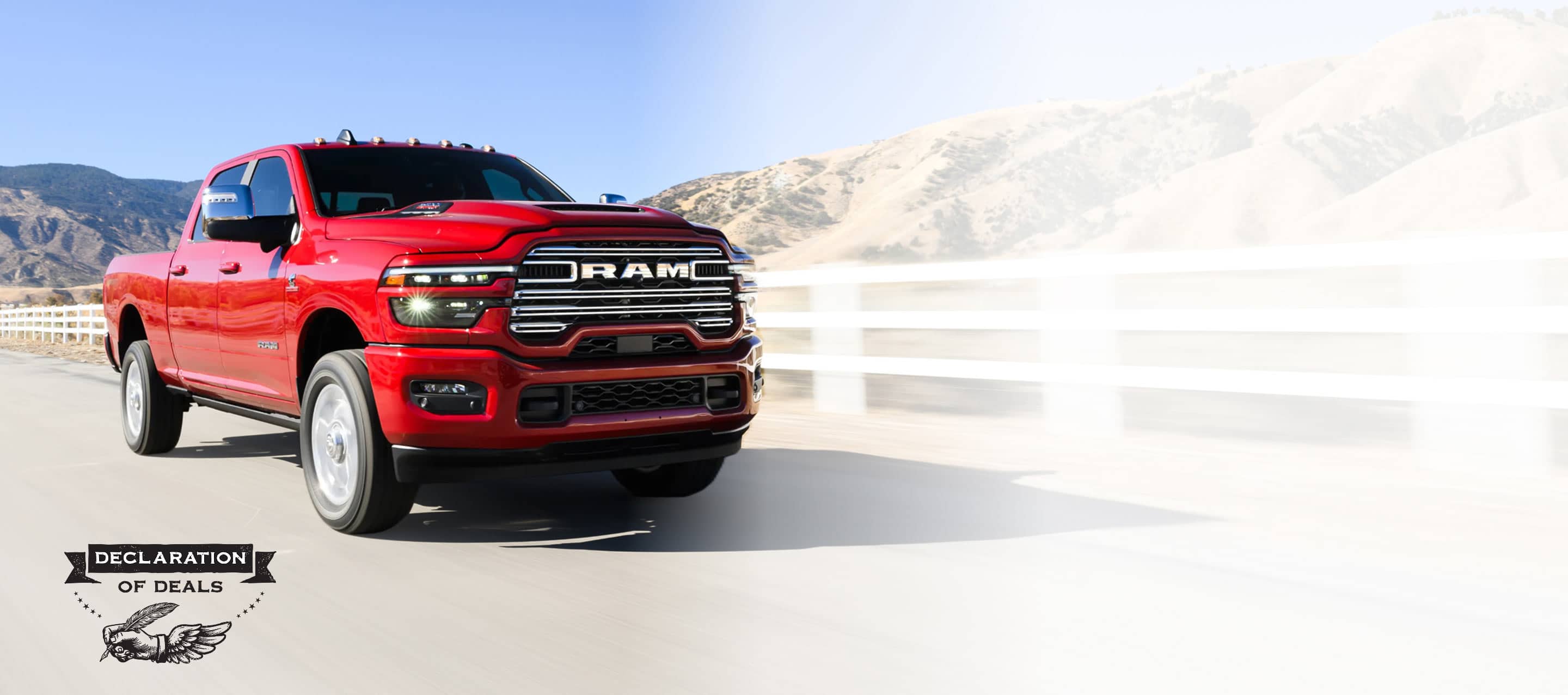 A red 2025 Ram 2500 Laramie 4x4 Crew Cab traveling on a highway beside a ranch in the desert. Declaration of Deals Sales Event.