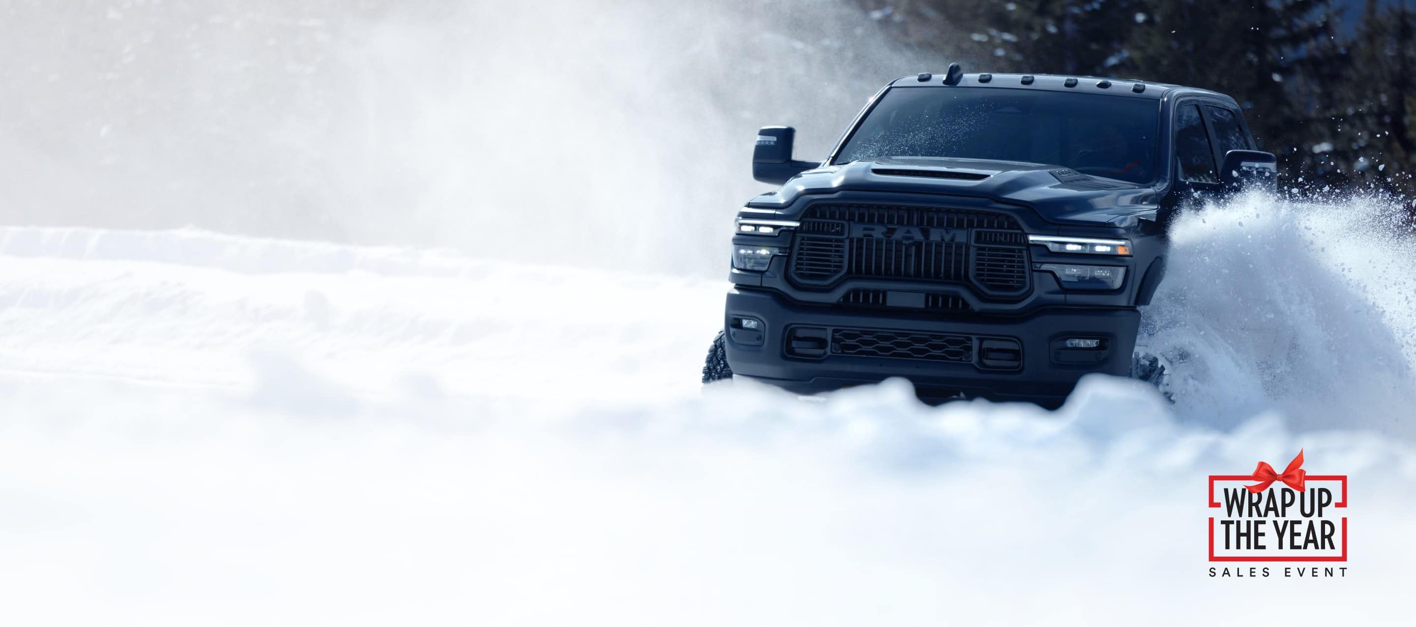A gray 2025 Ram 2500 Rebel 4x4 Crew Cab traveling through deep snow in a forest. Wrap Up The Year Sales Event.