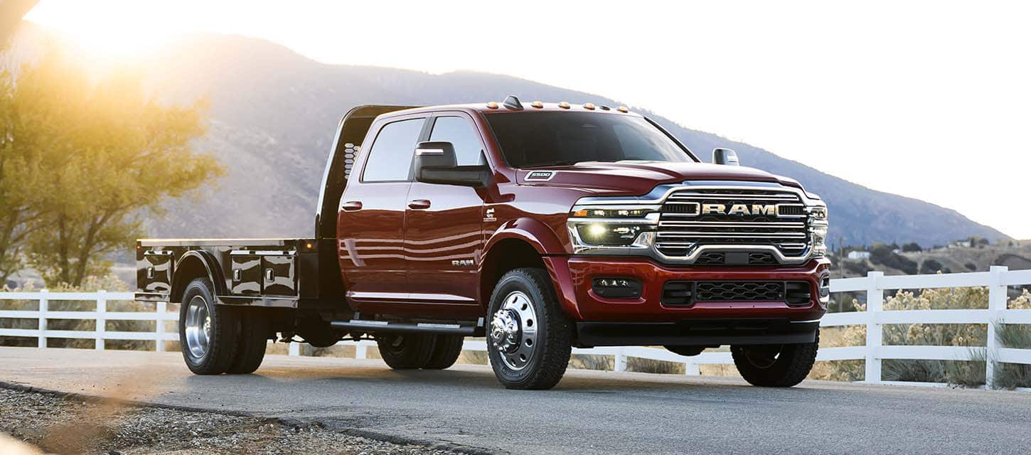 A red 2025 Ram 5500 Laramie Chassis Cab Crew Cab with a platform upfit, traveling down a country road.