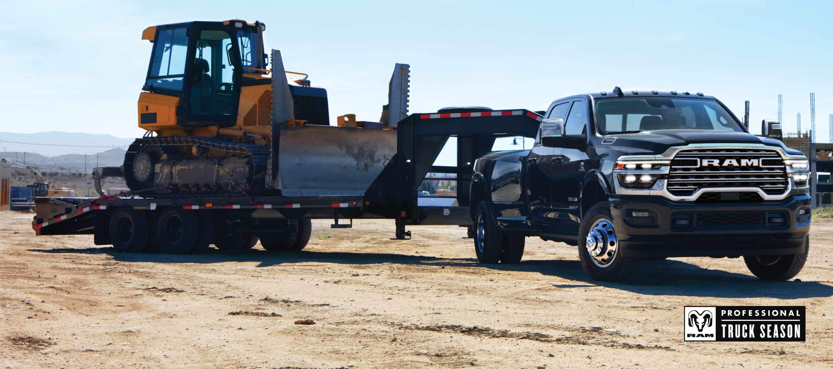 A black 2025 Ram 3500 4x4 Crew Cab towing an excavator on a fifth wheel flatbed trailer through a construction site. Ram Professional Truck Season.