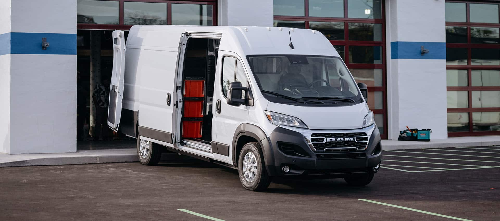 A white 2025 Ram ProMaster EV 3500 SLT High Roof Cargo Van with its passenger-side sliding door and rear doors open, revealing crates on shelves.