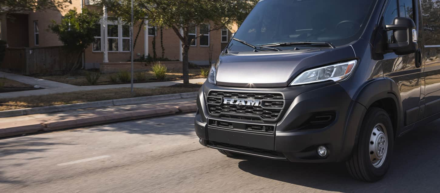 A black 2025 Ram ProMaster 2500 Tradesman Cargo Van High Roof being driven through a residential neighborhood.