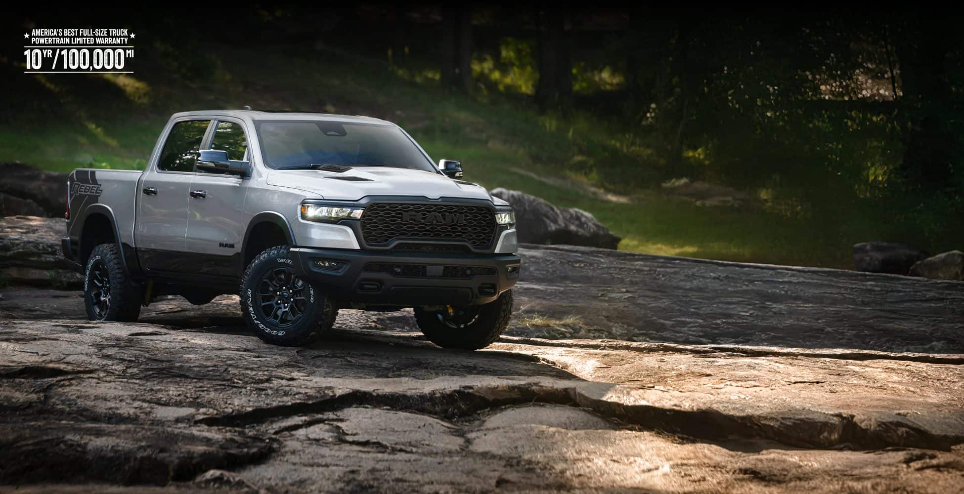 A silver 2026 Ram 1500 Rebel 4x4 Crew Cab traveling across an uneven trail off-road. America’s best full-size truck powertrain limited warranty 10yr/ 100,000mi.