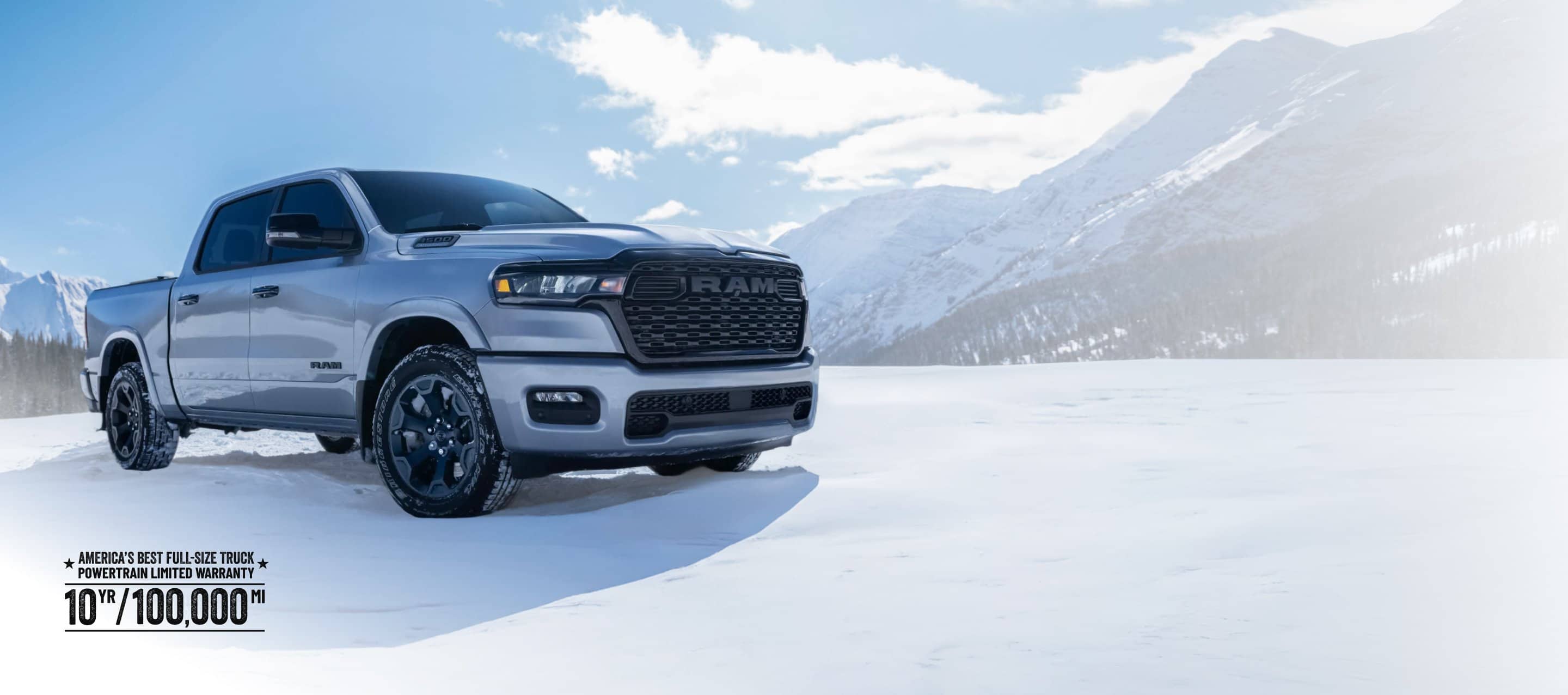 A white 2026 Ram 1500 Big Horn 4x4 Crew Cab parked on a snow-covered clearing off-road in the mountains. Limited warranty 10yr/ 100,000mi.