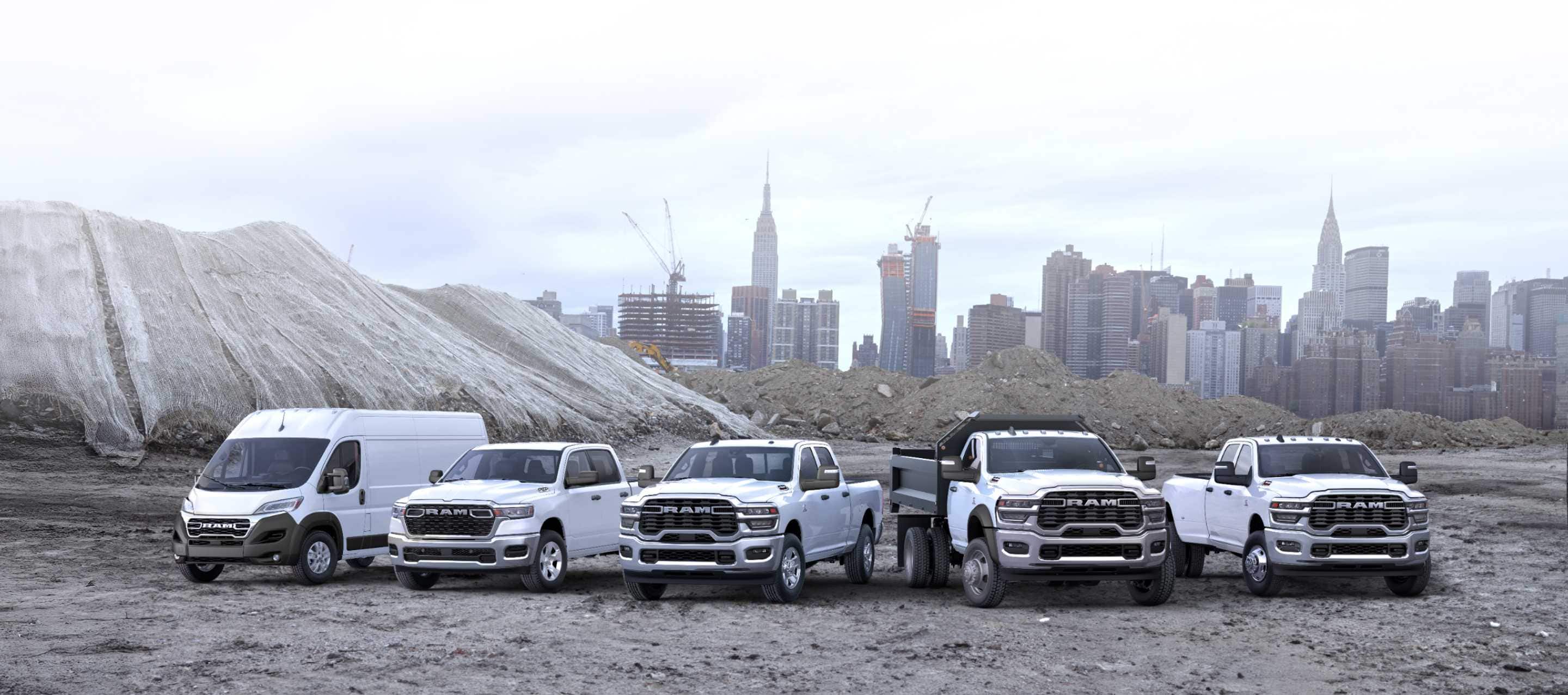 A lineup of Ram trucks and vans, all in white at a commercial construction site. From left to right: a Ram ProMaster 3500 SLT High Roof Cargo Van, a Ram 1500 Tradesman 4x4 Crew Cab, a Ram 2500 Tradesman 4x4 Crew Cab, a Ram 4500 Big Horn Regular Cab Chassis Cab with a dump body upfit and a Ram 3500 Tradesman 4x4 Crew Cab. Ram Professional.