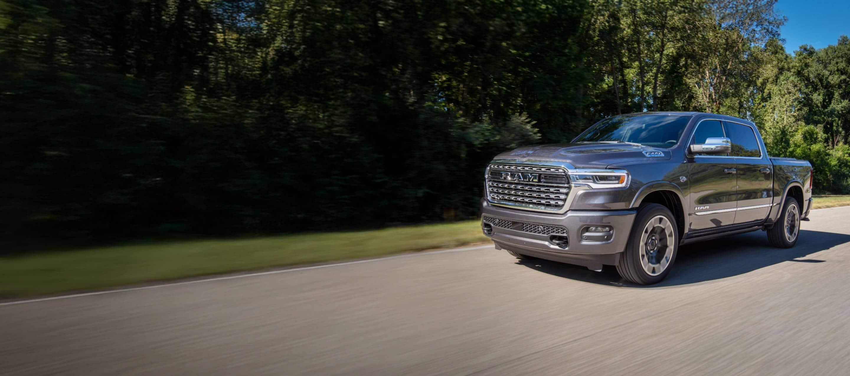 A gray 2026 Ram 1500 Limited 4x4 Crew Cab traveling down a country road.