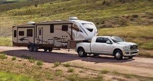 A white 2024 Ram 3500 Limited Mega Cab towing a huge fifth wheel travel trailer as it is driven down a mountain road.