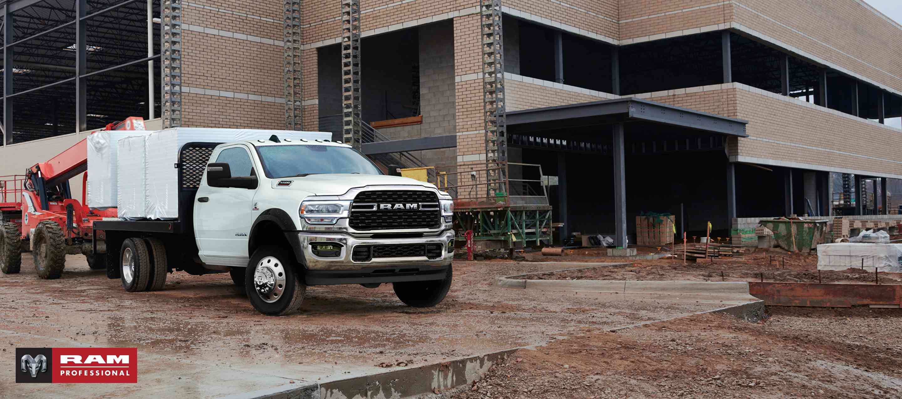 A white 2024 Ram Chassis Cab with a platform upfit loaded with building materials, parked at a commercial construction site. Ram Professional.