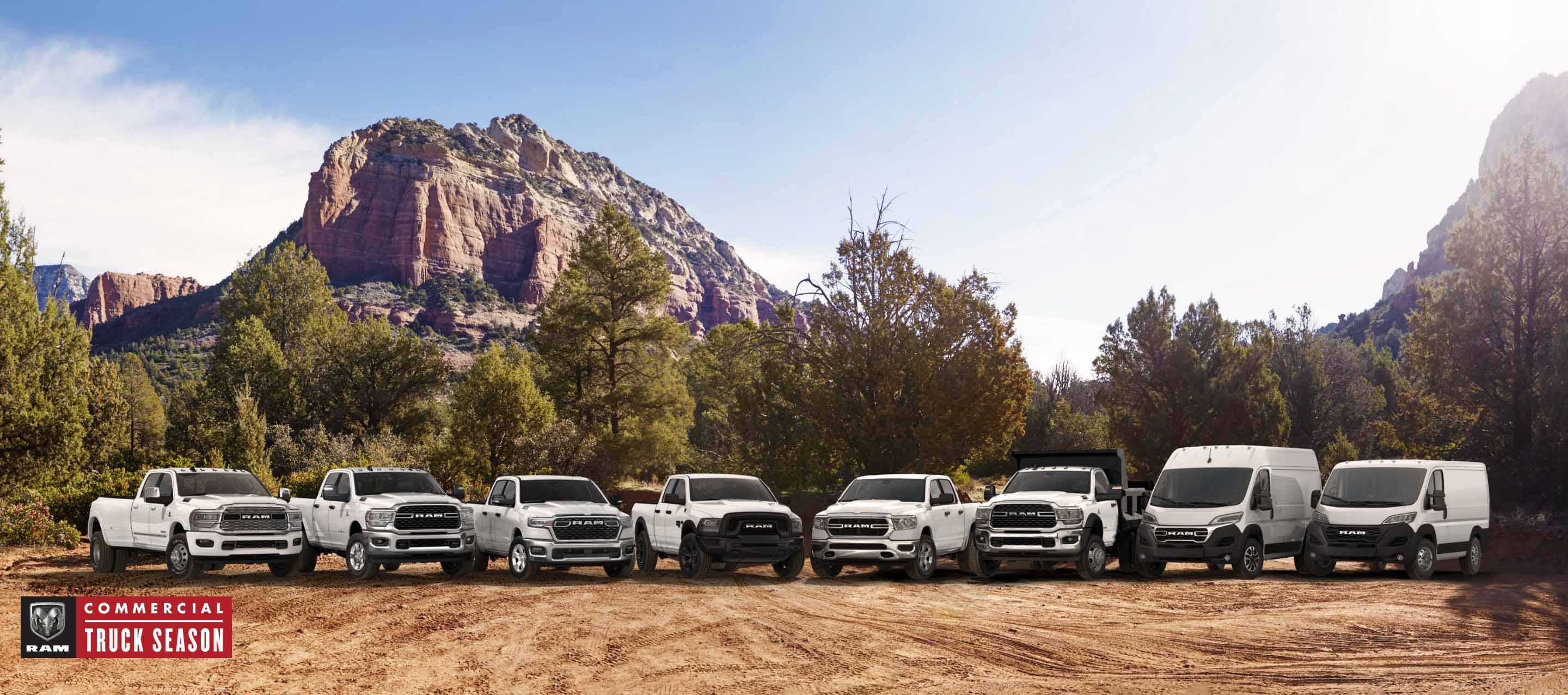 The Ram Brand lineup, all in white, parked side-by-side on a clearing, with mountains in the background. From left to right: a 2024 Ram 3500 Limited Crew Cab, a 2024 Ram 2500 Big Horn Crew Cab, a 2025 Ram 1500 Big Horn Crew Cab, a 2024 Ram 1500 Classic Warlock Quad Cab, a 2024 Ram 1500 Tradesman Crew Cab, a Ram 5500 Tradesman Chassis Cab Regular Cab with dump body upfit, a 2024 Ram ProMaster 1500 SLT+ High Roof Cargo Van and a 2024 Ram ProMaster 1500 Tradesman Standard Roof Cargo Van. Ram Commercial Truck Season.