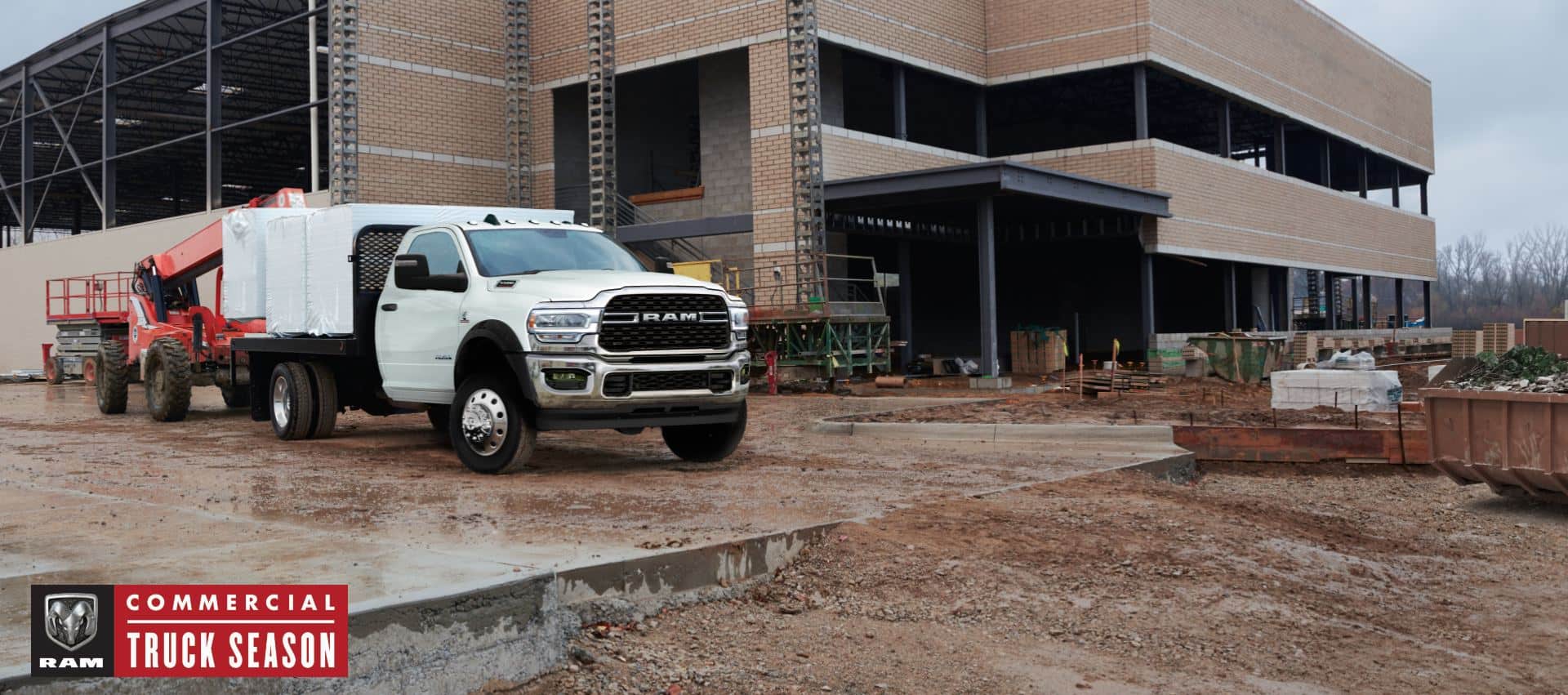 A white 2024 Ram Chassis Cab with a platform upfit loaded with building materials, parked at a commercial construction site. Commercial Truck Season.